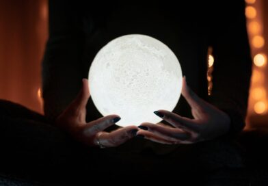 A person holding a glowing moon lamp, surrounded by warm bokeh lights, creating a mystical indoor atmosphere.