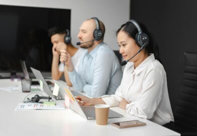 Call center agents wearing headsets working on laptops at a customer support team meeting.