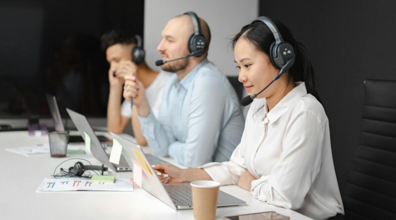 Call center agents wearing headsets working on laptops at a customer support team meeting.