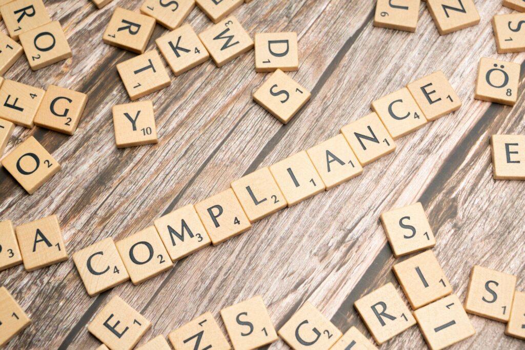 The word compliance spelled out with wooden letter tiles on a rustic table