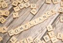 The word compliance spelled out with wooden letter tiles on a rustic table