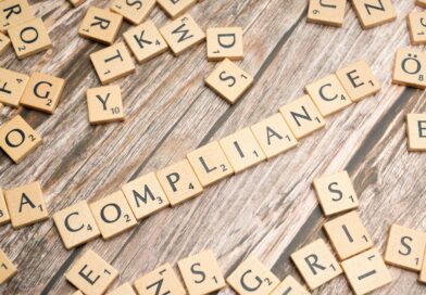 The word compliance spelled out with wooden letter tiles on a rustic table
