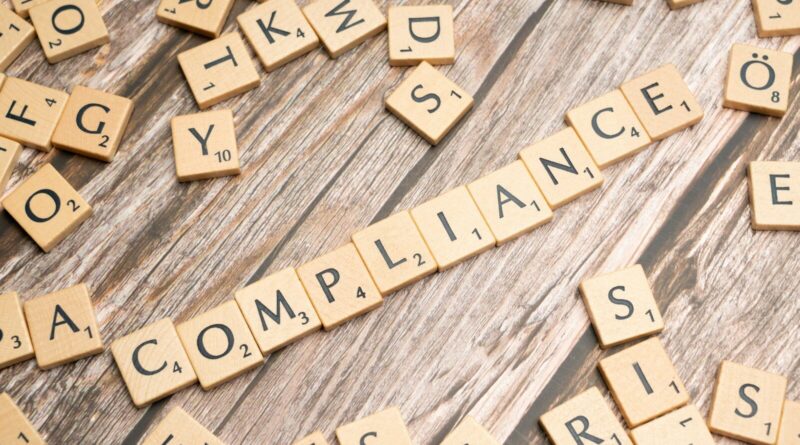 The word compliance spelled out with wooden letter tiles on a rustic table